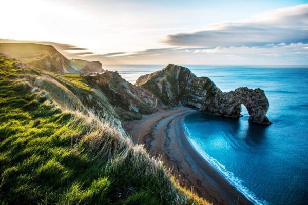 Coastal cliffs overlooking a crescent beach and sea arch above turquoise water
