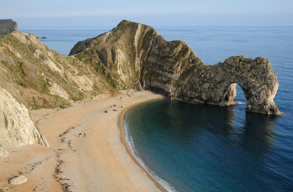 Secluded sandy cove with steep cliffs and a natural sea arch over calm blue water