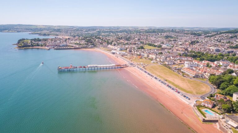 Aerial view of a seaside town with a long pier, sandy beach, and calm blue water